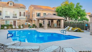 A swimming pool with lounge chairs, a covered patio, and a stone facade building.
