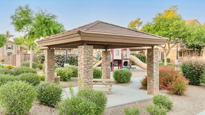 A gazebo with a stone base and a tiled roof, surrounded by landscaped gardens and a playground with slides.