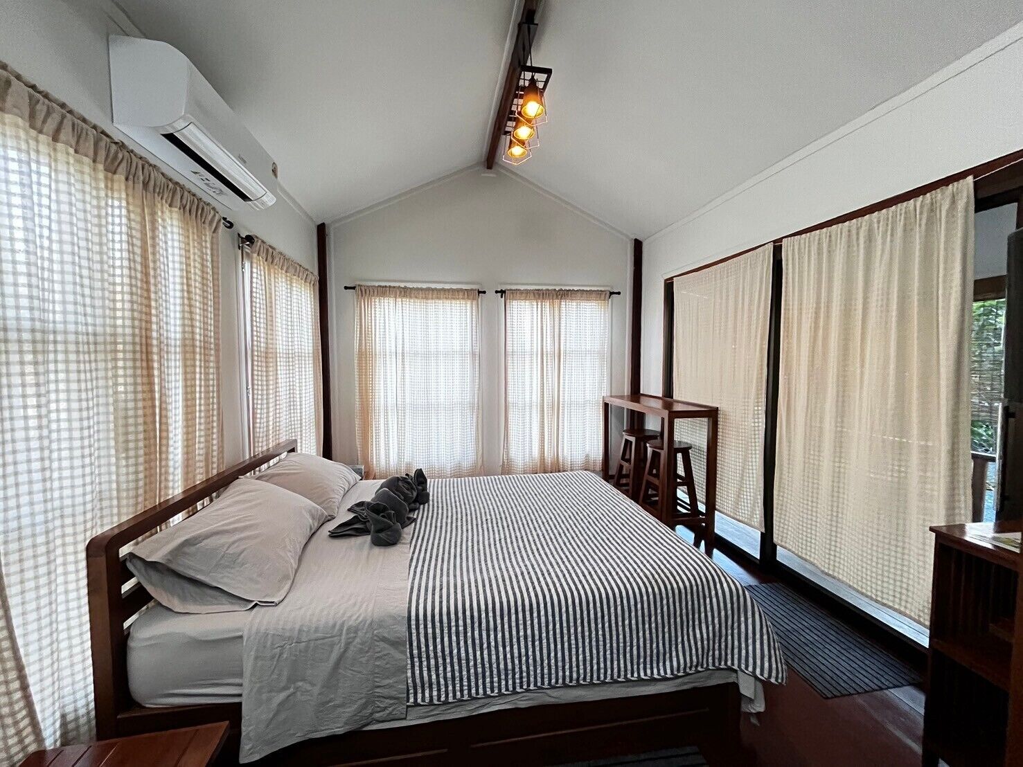 Une chambre à coucher avec un lit, des rideaux, une table de chevet en bois et un luminaire fixé au plafond.