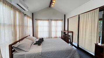 Une chambre à coucher avec un lit, des rideaux, une table de chevet en bois et un luminaire fixé au plafond.