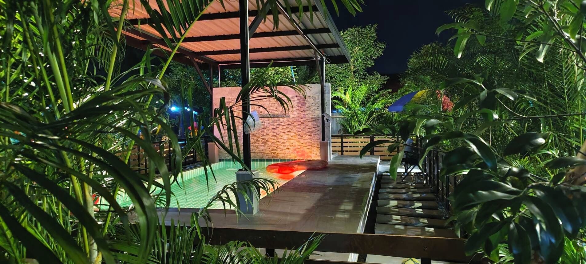 A covered outdoor area with a pool, surrounded by lush greenery and a brick wall.