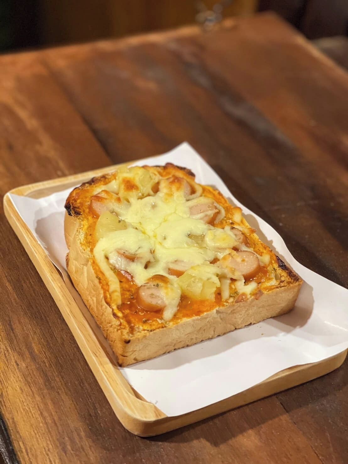 En rektangulær pizza på et stykke hvidt papir på et træbord.