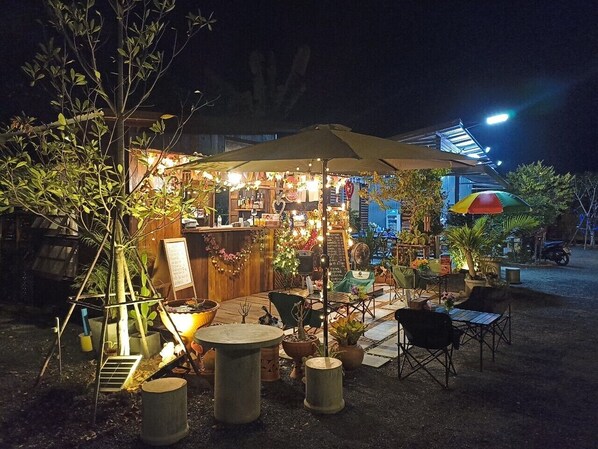 An outdoor café with tables and chairs, a wooden structure in the background, and a street lamp.
