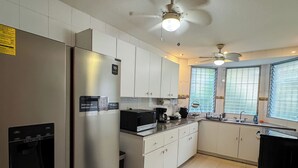 A modern kitchen with a stainless steel refrigerator, white cabinets, a built-in oven, and a ceiling fan.