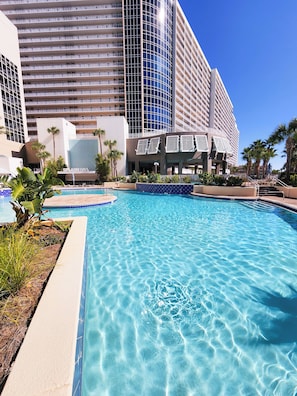 Un hotel con piscina, palmeras y un edificio moderno con balcones.