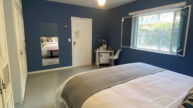 Un dormitorio con cama, escritorio, silla, ventilador de techo y ventana con vistas al exterior.