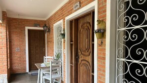 Fachada de ladrillo con dos puertas de madera, un portón de metal y una mesa con sillas afuera.