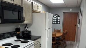 A kitchen with white appliances, wooden cabinets, a dining table with chairs, and a window with a decorative frame. - CLEARFORK CREEK LODGING & RV CAMPGROUND#4 (LaFollette)