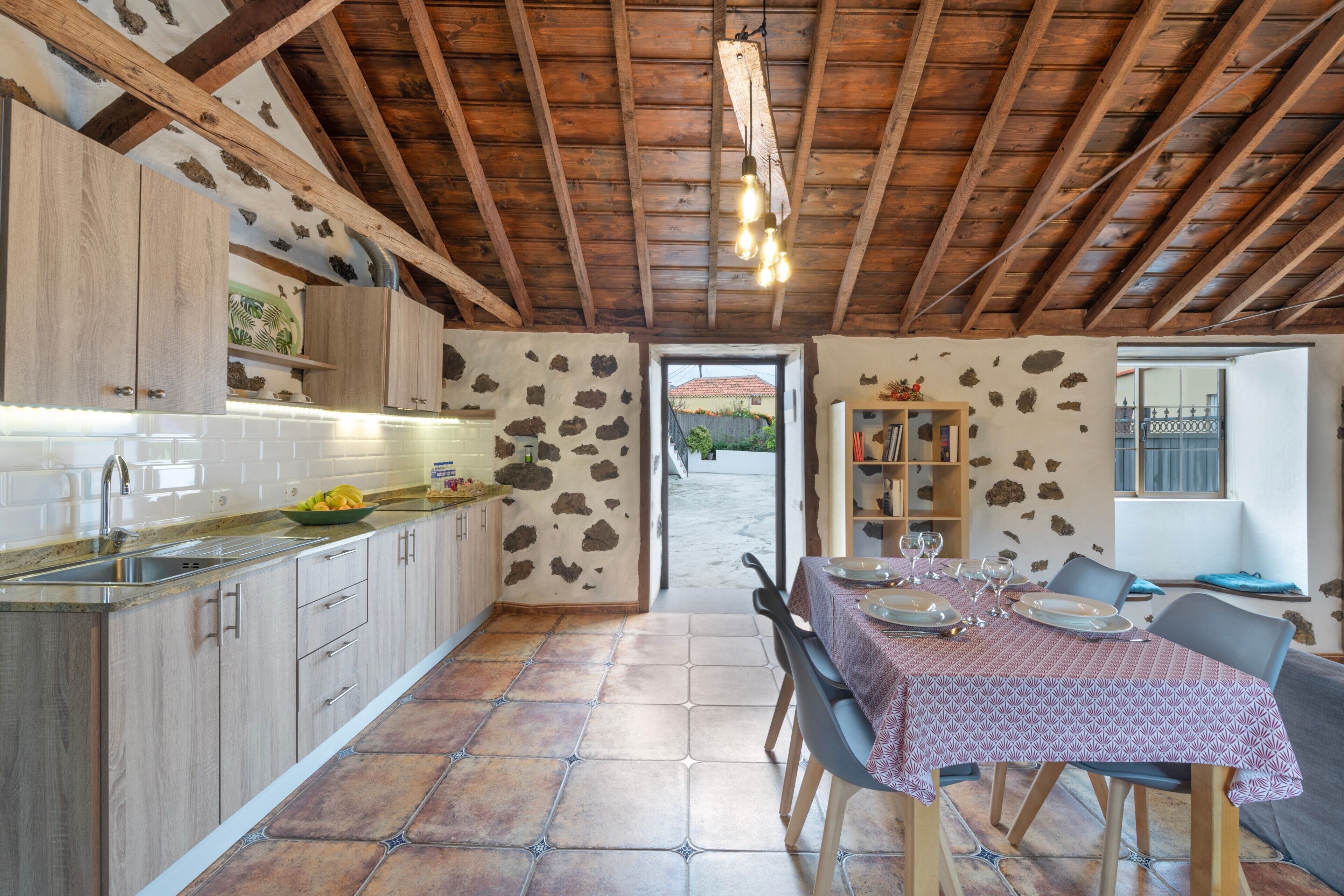Cucina rustica con travi in legno, parete in pietra e zona pranzo con tavolo apparecchiato per due.