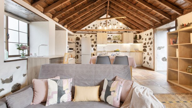 A cozy living room with a sofa, a dining area with chairs, a kitchen with a refrigerator, and a stone wall. - Holiday Home 'Estudio Bibi' with Mountain Views and Private Terrace (El Paso)