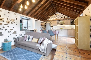 A cozy interior with a wooden ceiling, a sofa, a dining area, and a kitchen.
