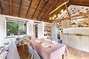 A dining area with a table set for four, a kitchen with a stone floor, and a wooden ceiling.