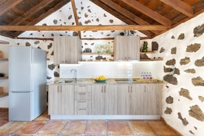 A kitchen with a stone wall, wooden cabinets, a refrigerator, and a tiled floor.