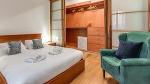 A bedroom with a bed, a green armchair, a wooden wardrobe, and a walk-in closet.
