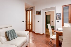 Ein Wohnzimmer mit einem weißen Sofa, einem Esstisch mit Stühlen, einer Holztür und einem Bild an der Wand.