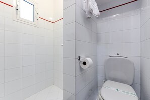 Ein Badezimmer mit weißen Fliesen, einer Toilette, einem Handtuchhalter und einem Fenster mit rotem Rahmen.