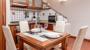 A kitchen with wooden cabinets, a tiled backsplash, a dining table set with plates and glasses, and a microwave.