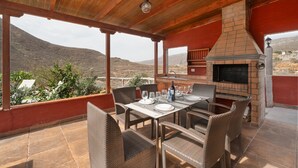Un espace extérieur aménagé pour les repas, avec un four en briques, des meubles en osier et une vue sur le paysage.