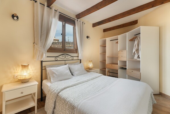 A bedroom with a bed, bedside lamps, a window with curtains, a wardrobe, and a nightstand.