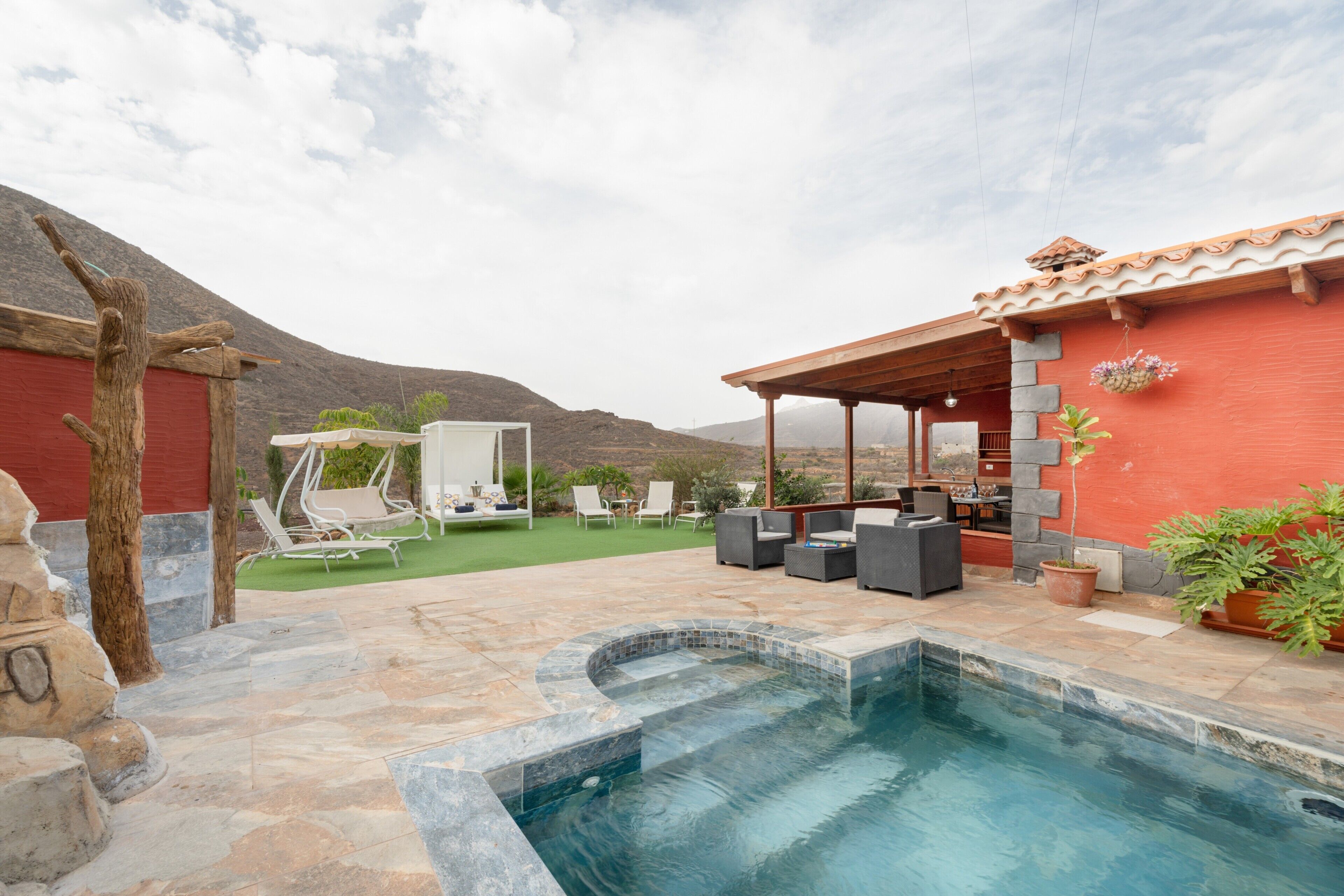 A swimming pool with a stone deck, outdoor seating, and a red building with stone accents.