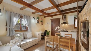 Un salon chaleureux avec un canapé, une table à manger et des chaises, une cuisine équipée d’une cuisinière et un mur en pierre.