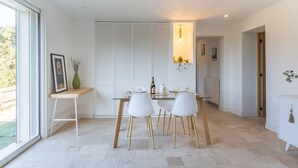 Un espace repas moderne avec une table en verre, des chaises blanches, une table d’appoint en bois et un meuble blanc.