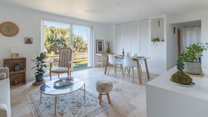 Un salon moderne avec une table basse en verre, un tapis à motifs, un buffet en bois et un coin repas comprenant des chaises blanches et une table en bois.