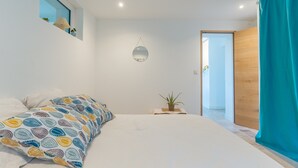 Une chambre avec un lit, un miroir suspendu, une plante en pot et une vue sur un couloir.