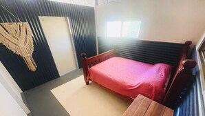 Een kleine, compacte kamer met een enkel bed, een houten nachtkastje, een deur en een raam.