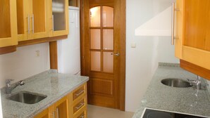 A kitchen with granite countertops, wooden cabinets, a stainless steel sink, and a frosted glass door.
