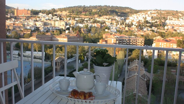 A balcony with a table set for tea, a view of a cityscape, and a building with a clock tower.