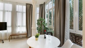 A room with a round table, a bench, a potted plant, a bottle of wine, and a TV. - Vacation Studio 'Estudio Esquina' with Shared Terrace, Wi-Fi and Air Conditioning (Las Palmas de Gran Canaria)
