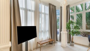 A room with a television on a stand, a bench, a potted plant, and large windows with curtains. - Vacation Studio 'Estudio Esquina' with Shared Terrace, Wi-Fi and Air Conditioning (Las Palmas de Gran Canaria)