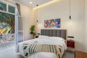 Une chambre d’hôtel moderne avec un grand lit, un balcon offrant une vue sur les palmiers et une peinture abstraite aux couleurs vives accrochée au mur.