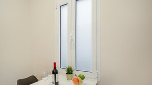 Ein Zimmer mit einem weißen Tisch, einer Weinflasche, einer Obstschale, einer Zimmerpflanze und einem Stuhl.