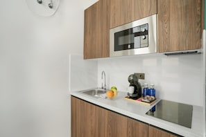 Une cuisine moderne équipée d’un four à micro-ondes en acier inoxydable, d’un four encastré, d’un évier et d’un plan de travail sur lequel se trouvent une machine à café et des bouteilles.