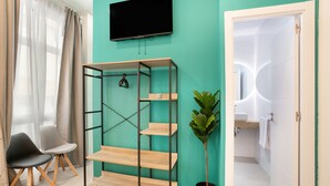 A room with teal walls, a TV mounted above a wooden shelf, a potted plant, a chair, and a door leading to a bathroom.