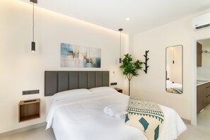 Een moderne hotelkamer met een groot bed, nachtkastjes, een wandspiegel en een plant.