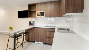 A modern kitchen with wooden cabinets, a built-in microwave, a stainless steel sink, and a flat-screen TV mounted on the wall.