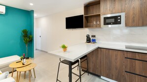 A modern kitchen with a white countertop, wooden cabinets, a built-in microwave, and a flat-screen TV.
