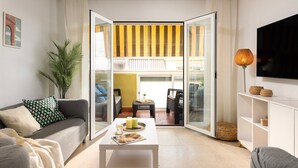 Ein Wohnzimmer mit einer Couch, einem Couchtisch und einem Fernseher. Eine Glastür führt auf einen Balkon.