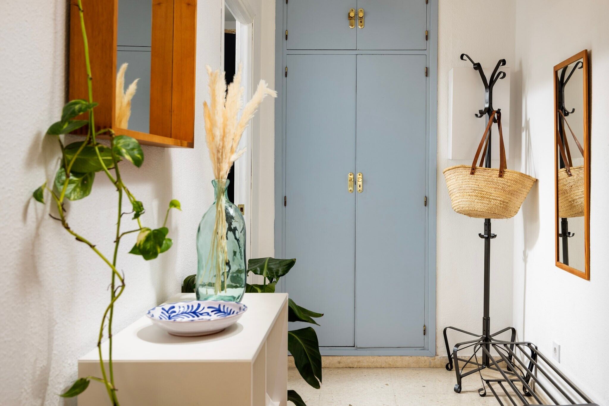 A hallway with a blue door, a white console table with a vase and plate, a floor lamp, and a mirror on the wall.