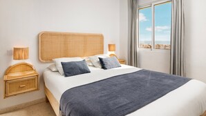 Ein Hotelzimmer mit einem großen Bett, zwei Nachttischen, einem Fenster mit Vorhängen und Blick auf die Stadt.