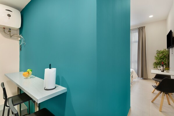 A modern room with teal walls, a white table, black chairs, a TV, and a plant.