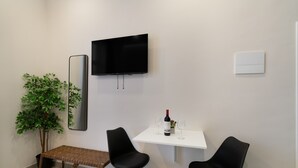 Une pièce moderne équipée d’un téléviseur, d’un banc, de deux chaises, d’une petite table avec une bouteille et des verres, et d’une plante en pot.