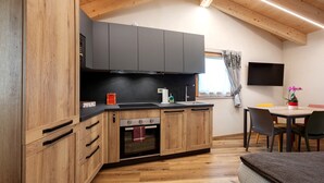 A kitchen with wooden cabinets, a black countertop, a built-in oven, and a dining area with chairs and a table. - Studio Apartment "La Chapelle - Sorreley" (Saint Christophe)