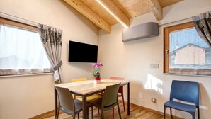 A dining area with a wooden table, chairs, a flat-screen TV, and a window with curtains. - Studio Apartment "La Chapelle - Sorreley" (Saint Christophe)
