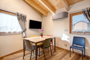 Ein Essbereich mit Holztisch, Stühlen, einem Flachbildfernseher und einem Fenster mit Vorhängen.