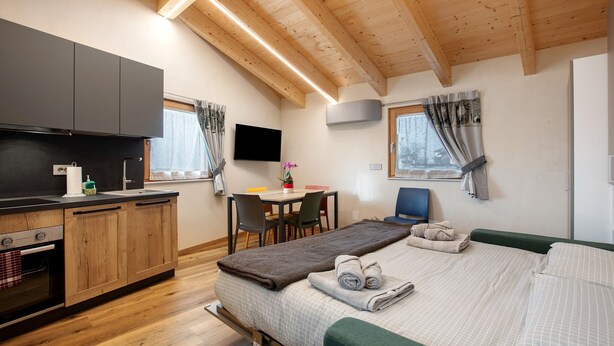 A room with a bed, a desk, a chair, a TV, and a kitchenette. - Studio Apartment "La Chapelle - Sorreley" (Saint Christophe)