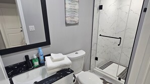 A modern bathroom with a white toilet, a black and white marble sink, a mirror, and a shower with a glass door. - Cozy 2 Bedrm with separate entrance
 (Kitchener)